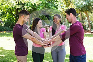 Cheerful multiracial men and women stacking hands during breast cancer awareness campaign