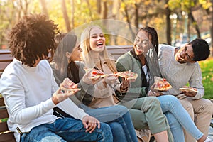 Cheerful multiracial teens laughing while eating pizza