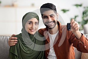 Cheerful Muslim Couple Showing New Car Key Sitting At Home