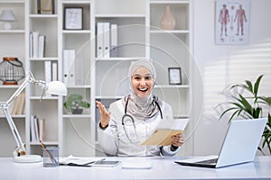 Cheerful muslim female doctor in hijab consulting patients in clinic office