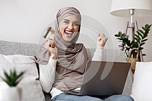 Cheerful Muslim Girl Celebrating Success With Credit Card And Laptop