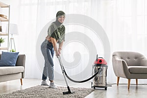 Cheerful muslim woman cleaning rug carpet with vacuum cleaner