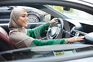 Cheerful muslim woman driving car, checking air conditioning