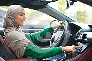 Cheerful muslim woman driving car, using dashboard