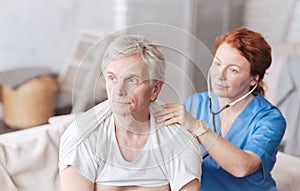 Cheerful nurse with stethoscope listening to lung sounds of patient