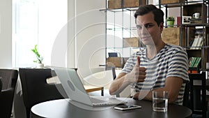 Cheerful office worker at desk doing thumb up sign and smiling. Real workplace