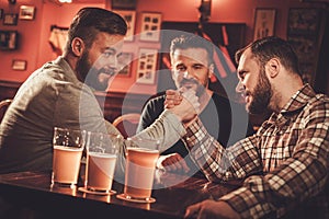 Cheerful old friends having arm wrestling challenge in a pub.