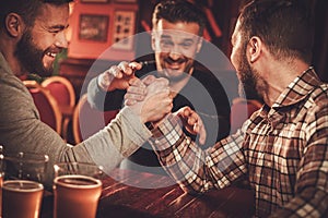 Cheerful old friends having arm wrestling challenge in a pub.