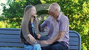 Cheerful old man cuddles granddaughter sitting on bench