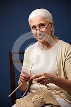 Cheerful old woman knitting. Looking camera.