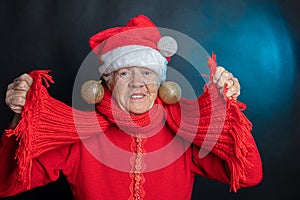 A cheerful, old woman, in a New Year`s cap, with a large present in her hands. Studio photo. Dark background