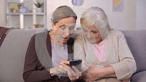 Cheerful old women watching photos on smartphone and laughing, good memories