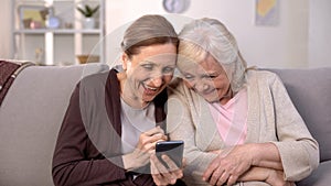 Cheerful old women watching photos on smartphone laughing, good memories, fun