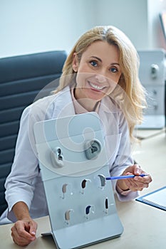 Cheerful otorhinolaryngologist pointing with a pen at listening apparatuses