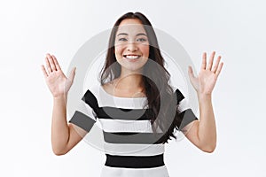 Cheerful outgoing young asian woman saying hi and smiling friendly, raising hands waiting in greeting or goodbye