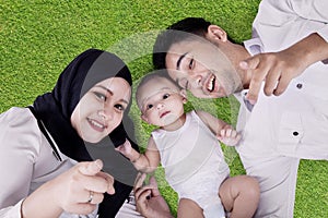 Cheerful parents and cute baby lying on grass