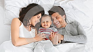 Cheerful parents having fun with their baby boy in bed