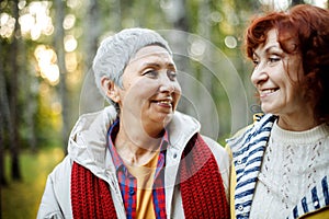 Cheerful pensioner female friends tallking and laughing in the autumn park.
