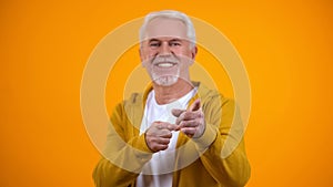 Cheerful pensioner showing hey you gesture, pointing fingers on camera, greeting