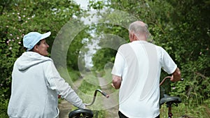 Cheerful pensioners, an old man and an elderly woman have fun on walk with bicycles, cute grandparents happily chat on