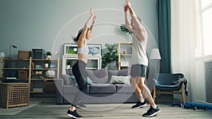 Cheerful people couple in sportswear doing sports jumping raising arms at home