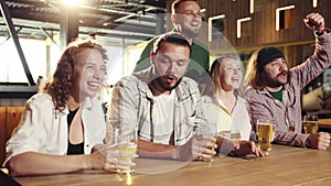 Cheerful people, friends sitting in bar, attentively watching football match translation, drinking beer, having fun