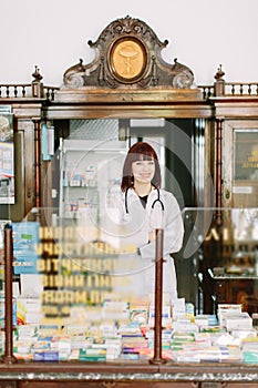 Cheerful pharmacist chemist woman standing in trading hall in vintage pharmacy drugstore