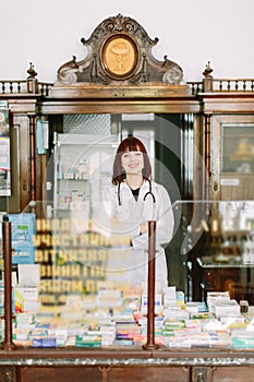 Cheerful pharmacist chemist woman standing in trading hall in vintage pharmacy drugstore