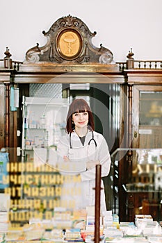 Cheerful pharmacist chemist woman standing in trading hall in vintage pharmacy drugstore