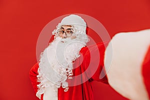 Cheerful photogenic Santa Claus is posing for a selfie, looking at the camera. Attractive man in Santa costume is taking selfie