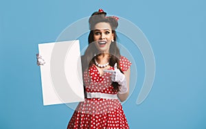 Cheerful pinup lady in retro outfit holding blank advertising board with copy space on blue background, mockup
