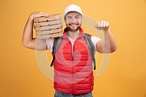 Cheerful pizza delivery man stands with carton boxes, waits for client, wears white cap and white tshirt with red waistcoat, poses