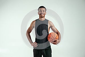 Cheerful player. Handsome young african man in sport clothing carrying a basketball ball and looking at camera with