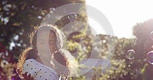 Cheerful, playful and happy little girl blowing bubbles in the garden at home. Smiling child playing outdoors on a