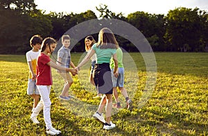 Cheerful playful preteen children in sunny summer park walking in circle holding hands.