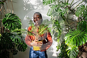 Cheerful pleased black woman plant lover holding Cycas plant in yellow pot in hands look at camera