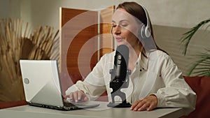 Cheerful podcaster woman recording her voice into a microphone. A female radio presenter broadcasts a podcast using a