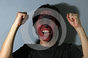 Cheerful portrait of a man with the flag of the Albania painted on his face on grey background.