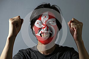 Cheerful portrait of a man with the flag of the Hong kong painted on his face on grey background. The concept of sport.