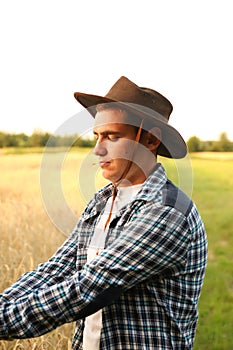 A cheerful portrait of a young cowboy-farmer. Vertical. Profile. expertise and dedication to agriculture, with a blurred