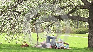 Cheerful portrait of a young family. Parents with their children lie under a blossoming apple tree. Family having fun on