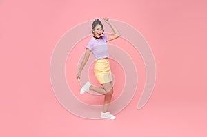 Cheerful positive Asian girl jumping in the air with raised fists looking at camera isolated on pink background