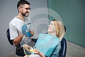 Cheerful positive dentist and client in dentistry. They look at each other and smile. Female client sit in chair and