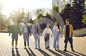 Cheerful positive multiracial friends holding hands standing in row on city street.