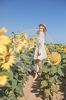 Cheerful positive young woman posing on camera among field of sunflowers. Happy girl  in straw hat during summertime. Harvest