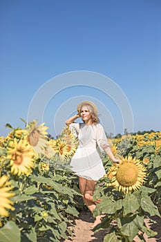 Cheerful positive young woman posing on camera among field of sunflowers. Happy girl  in straw hat during summertime. Harvest