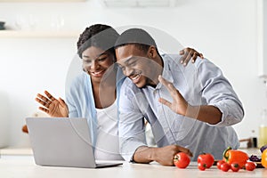 Cheerful pregnant black couple having video call while cooking