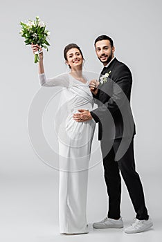 Cheerful pregnant bride holding bouquet near