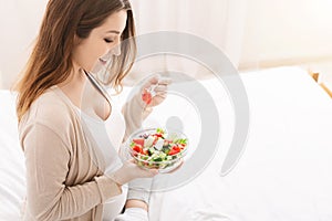 Cheerful pregnant lady dining with fresh healthy salad at home