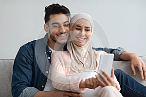 Cheerful Pregnant Middle Eastern Spouses Browsing Internet On Smartphone Together At Home